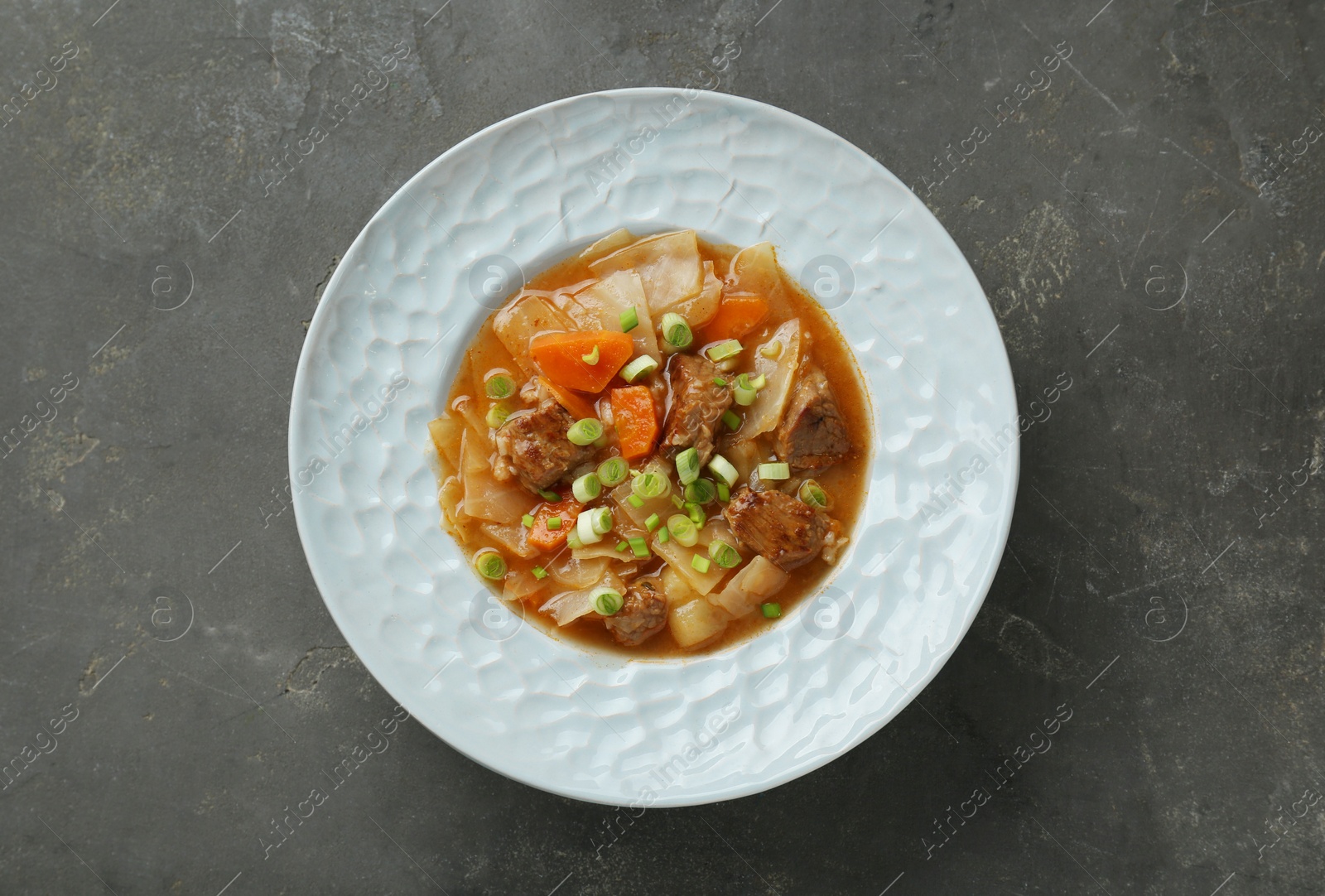 Photo of Tasty cabbage soup with meat, green onion and carrot on grey table, top view