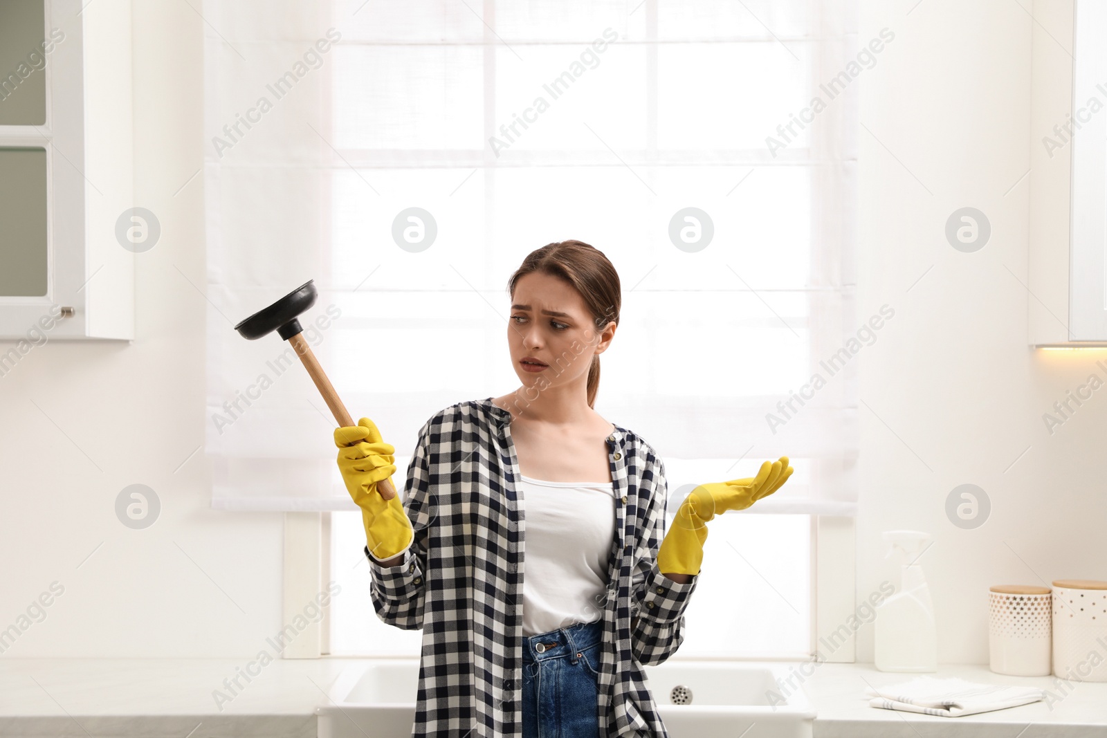 Photo of Overwhelmed young woman with plunger in kitchen