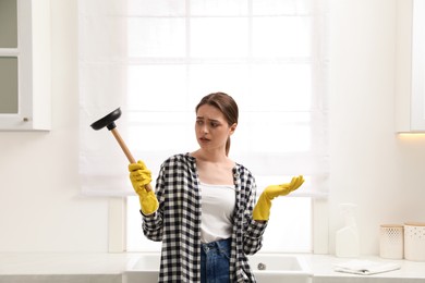 Photo of Overwhelmed young woman with plunger in kitchen
