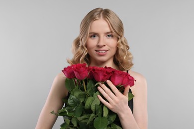 Photo of Beautiful woman with blonde hair holding bouquet of red roses on light grey background