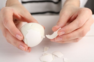 Photo of Woman peeling shell off boiled egg at white wooden table, closeup