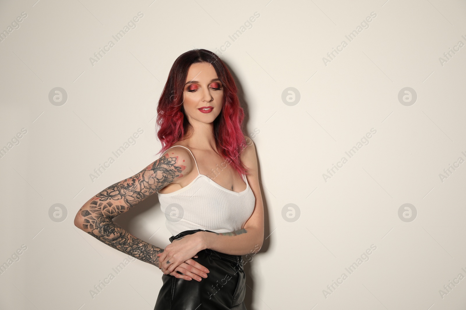 Photo of Beautiful woman with tattoos on arms against light background. Space for text