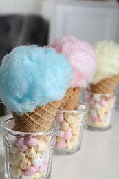 Photo of Sweet cotton candies in waffle cones and marshmallows on white table indoors, closeup