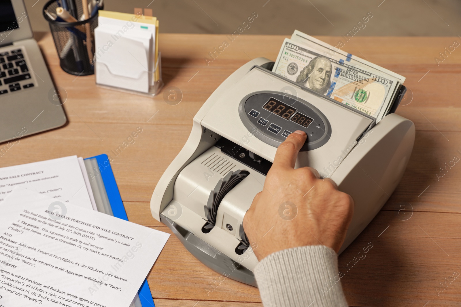 Photo of Man using banknote counter at wooden table indoors, closeup