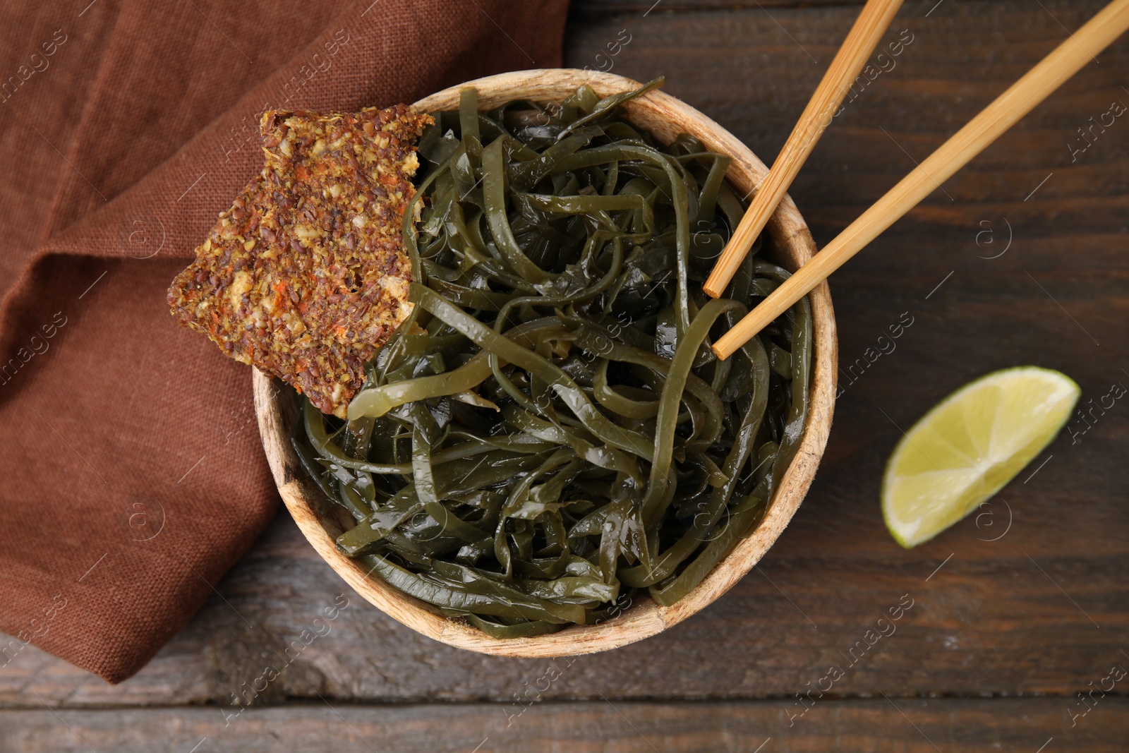 Photo of Tasty seaweed salad in bowl served on wooden table, flat lay