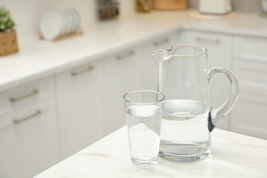 Photo of Jug and glass with clear water on white table in kitchen, space for text