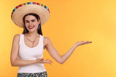 Photo of Young woman in Mexican sombrero hat showing something on yellow background. Space for text