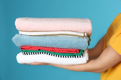 Young woman holding clean laundry on color background, closeup