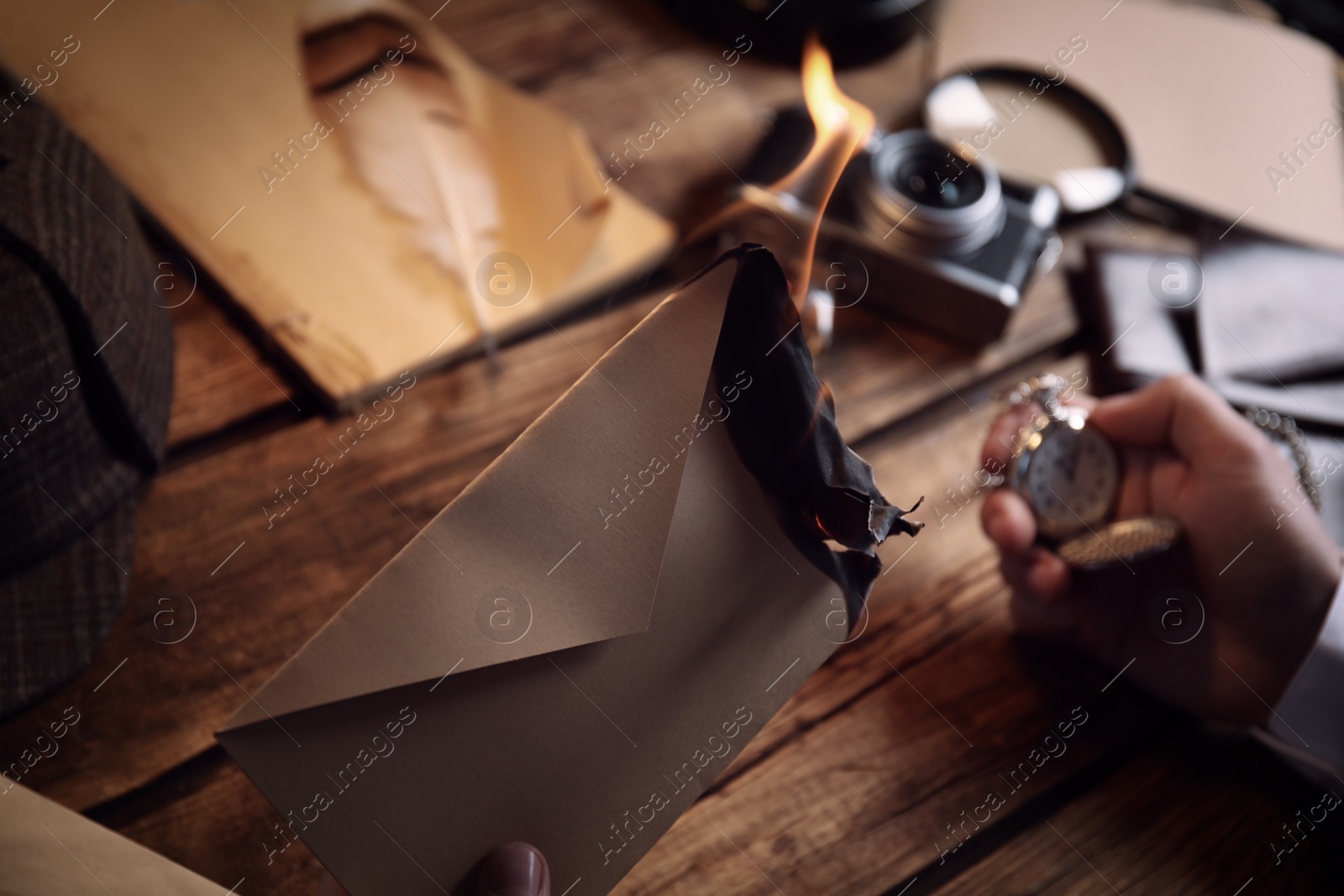 Photo of Detective with burning envelope and pocket watch at wooden table, closeup