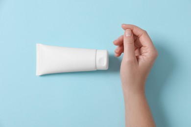 Woman with tube of hand cream on light blue background, top view