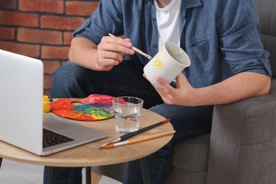 Photo of Man learning to decorate cup while watching online course indoors, closeup. Time for hobby