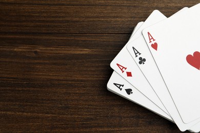 Photo of Four aces playing cards on wooden table, top view. Space for text