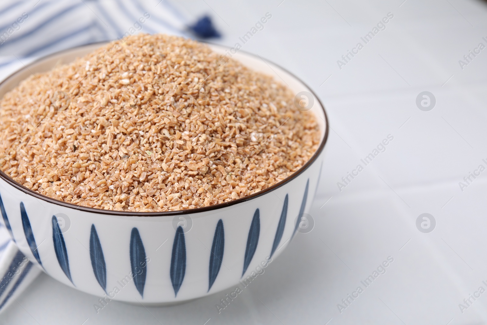 Photo of Dry wheat groats in bowl on white table, closeup. Space for text