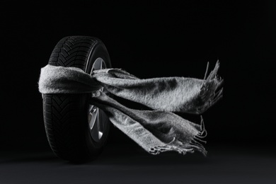 Photo of Winter tire with grey scarf on black background