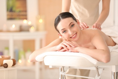 Beautiful young woman having massage with body scrub in spa salon