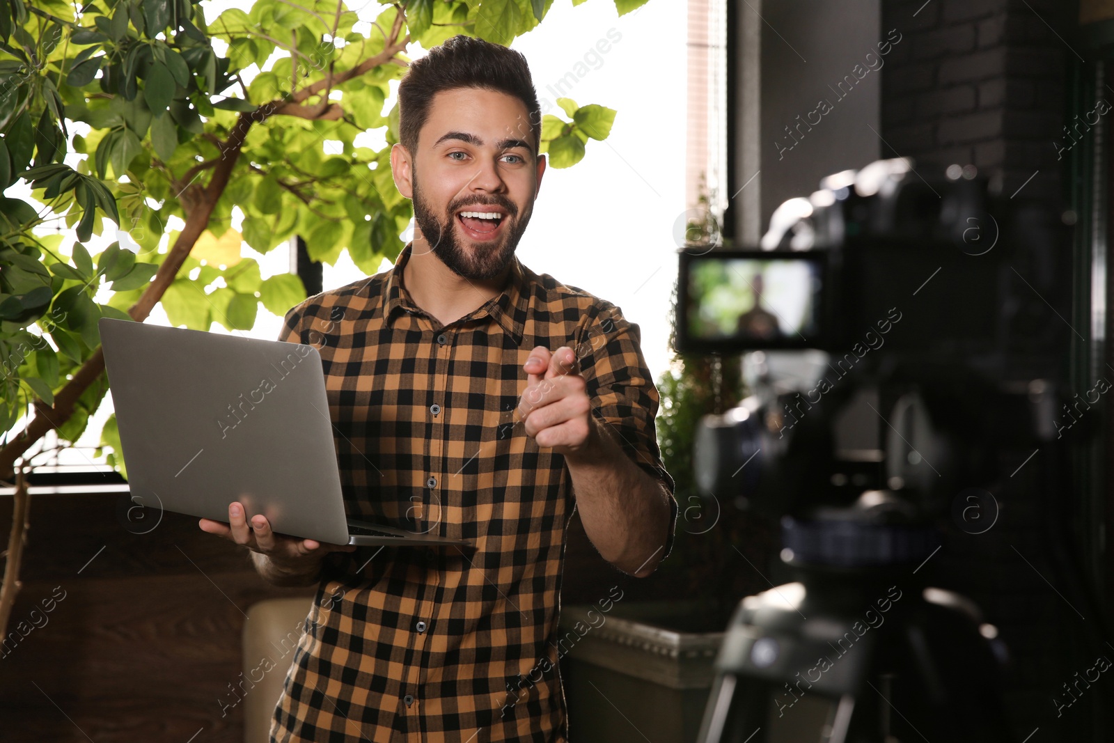 Photo of Young blogger with laptop recording video on camera indoors