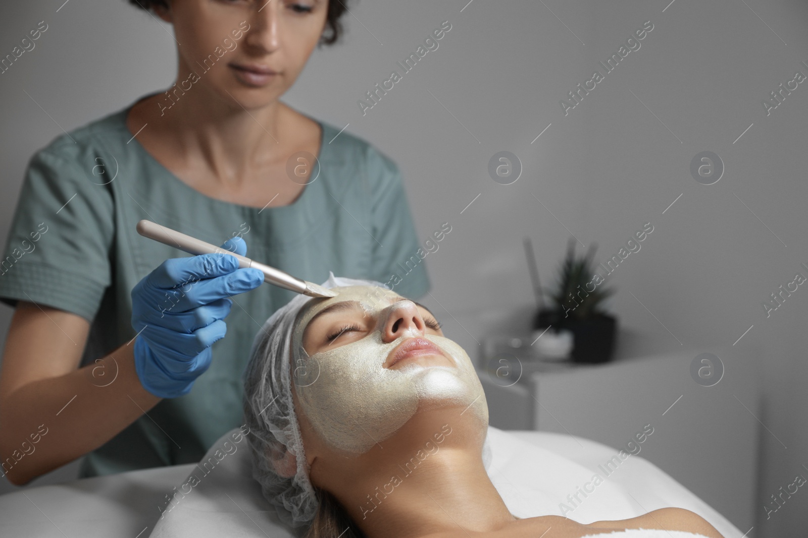 Photo of Cosmetologist applying mask on client's face in spa salon