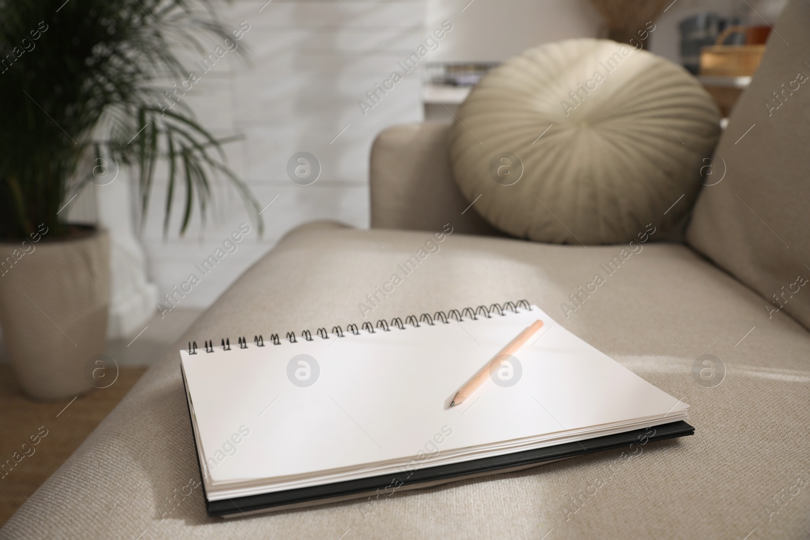 Photo of Notebook and pencil on light grey sofa in living room