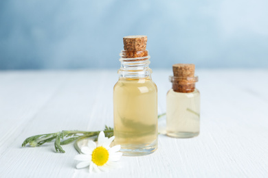 Photo of Bottles of essential oil and fresh chamomile on white wooden table