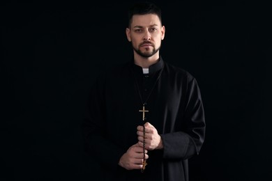 Priest with rosary beads on dark background