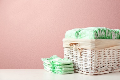 Photo of Wicker basket and disposable diapers on table against color background, space for text. Baby accessories