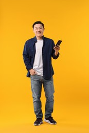 Photo of Full length portrait of happy man with smartphone on yellow background