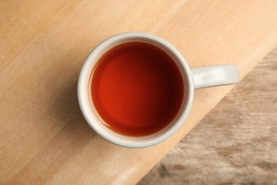 Photo of Cup of black tea on wooden board, top view