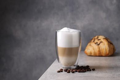 Photo of Aromatic latte macchiato in glass, coffee beans and croissant on light grey table. Space for text