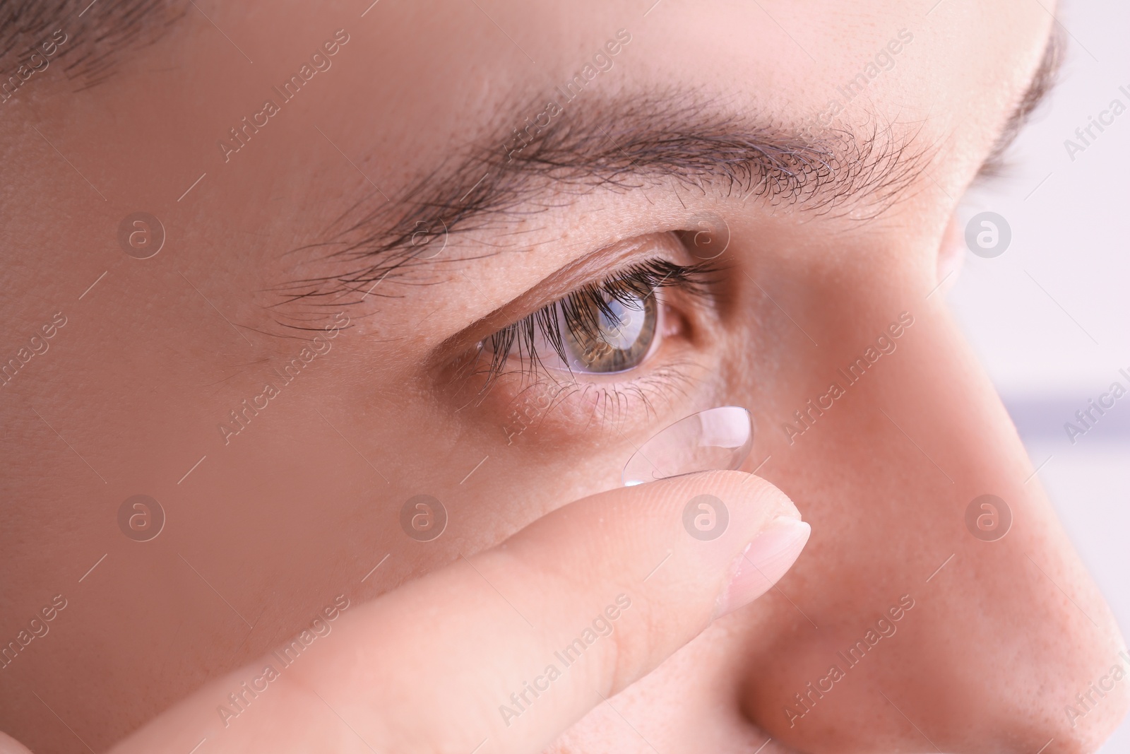 Photo of Young man putting contact lens in his eye, closeup