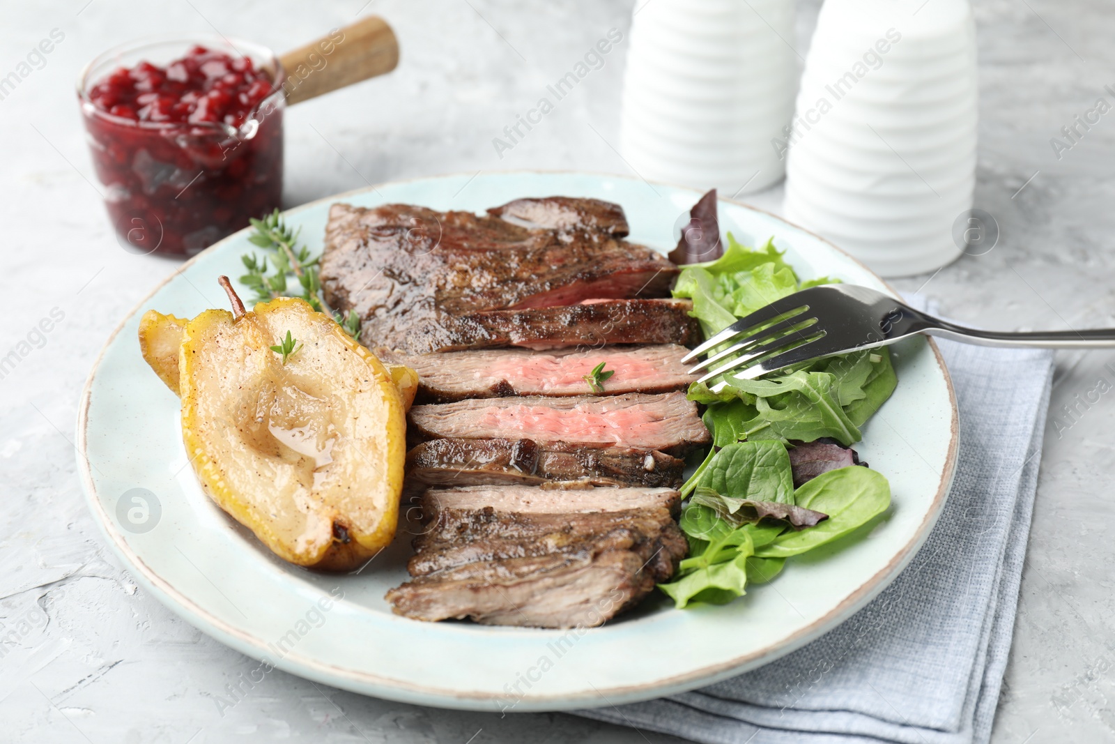 Photo of Delicious roasted beef meat, caramelized pear and greens served on light table, closeup