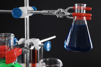 Photo of Retort stand and laboratory glassware with liquids on black background, closeup