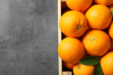 Photo of Wooden crate with ripe oranges on grey background, top view. Space for text