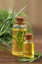 Bottles of essential oil and fresh tarragon leaves on wooden table