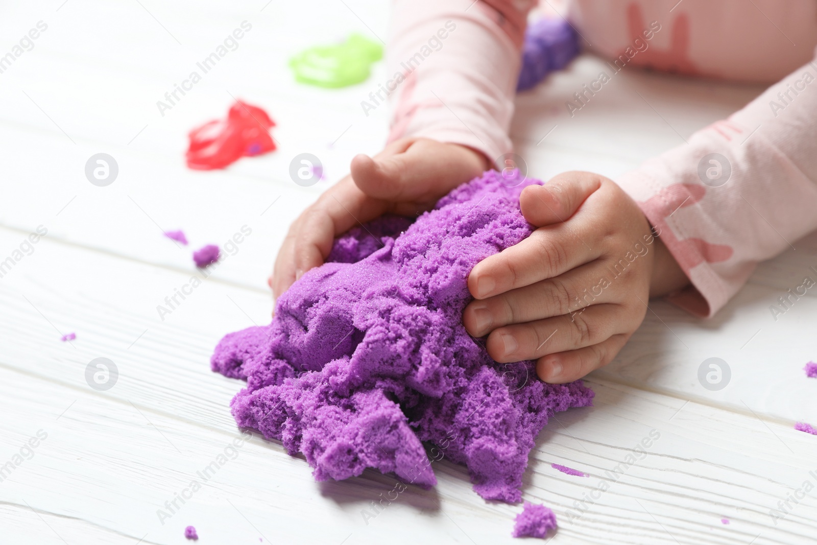 Photo of Little child playing with kinetic sand at white wooden table, closeup