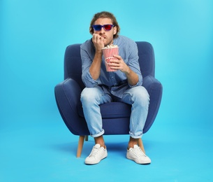 Photo of Emotional man with 3D glasses and popcorn sitting in armchair during cinema show on color background