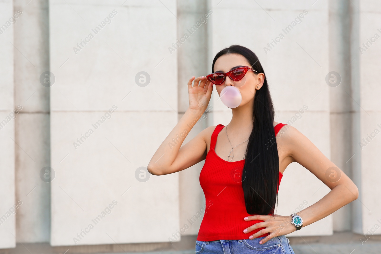 Photo of Beautiful woman in stylish sunglasses blowing gum near wall outdoors, space for text