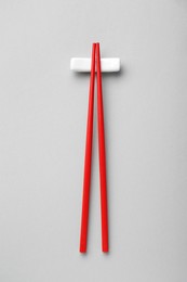 Photo of Pair of red chopsticks with rest on light grey background, top view