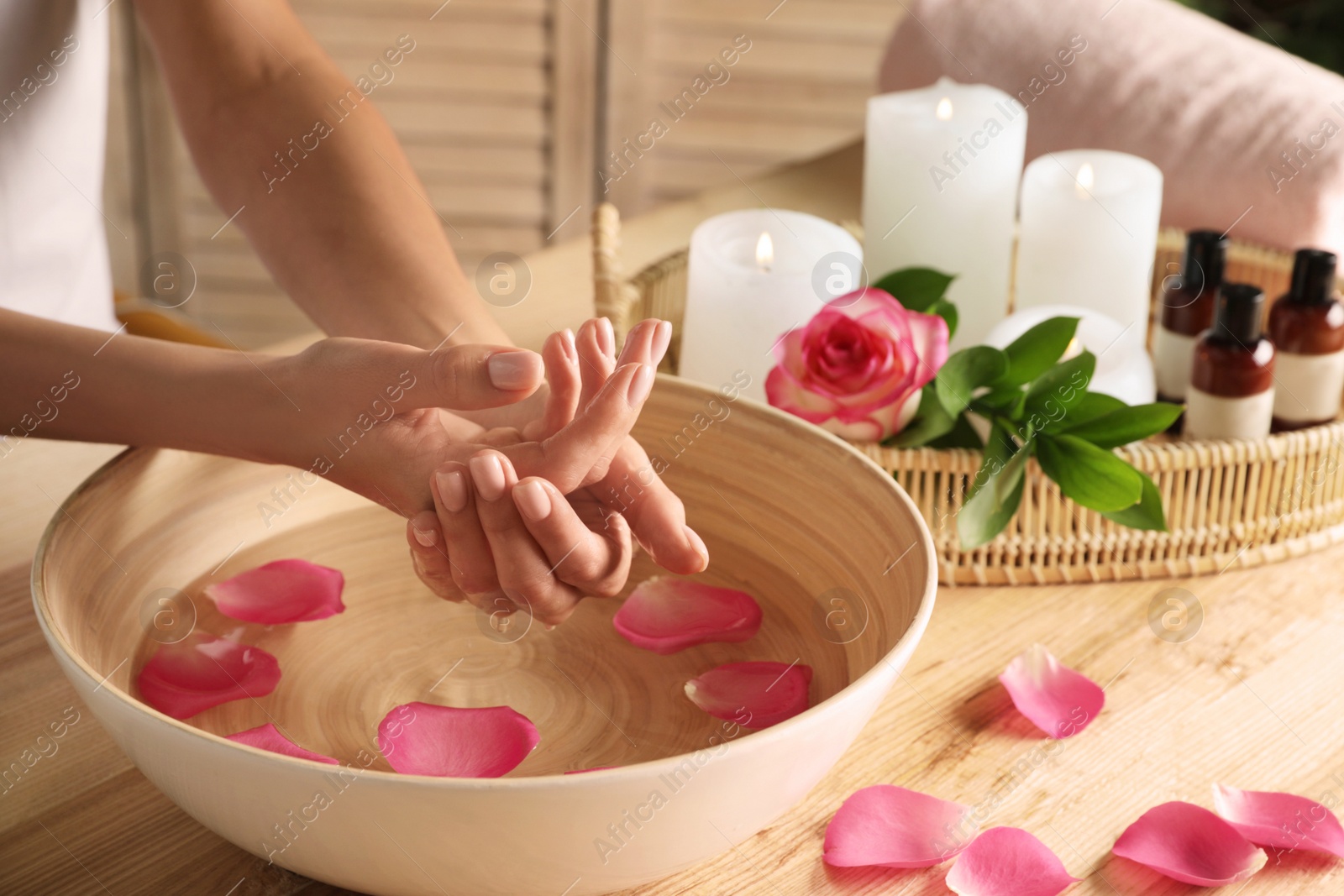 Photo of Woman soaking her hands in bowl of water and petals on table, closeup with space for text. Spa treatment