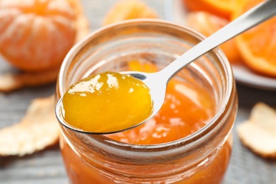 Teaspoon with tasty tangerine jam over jar, closeup