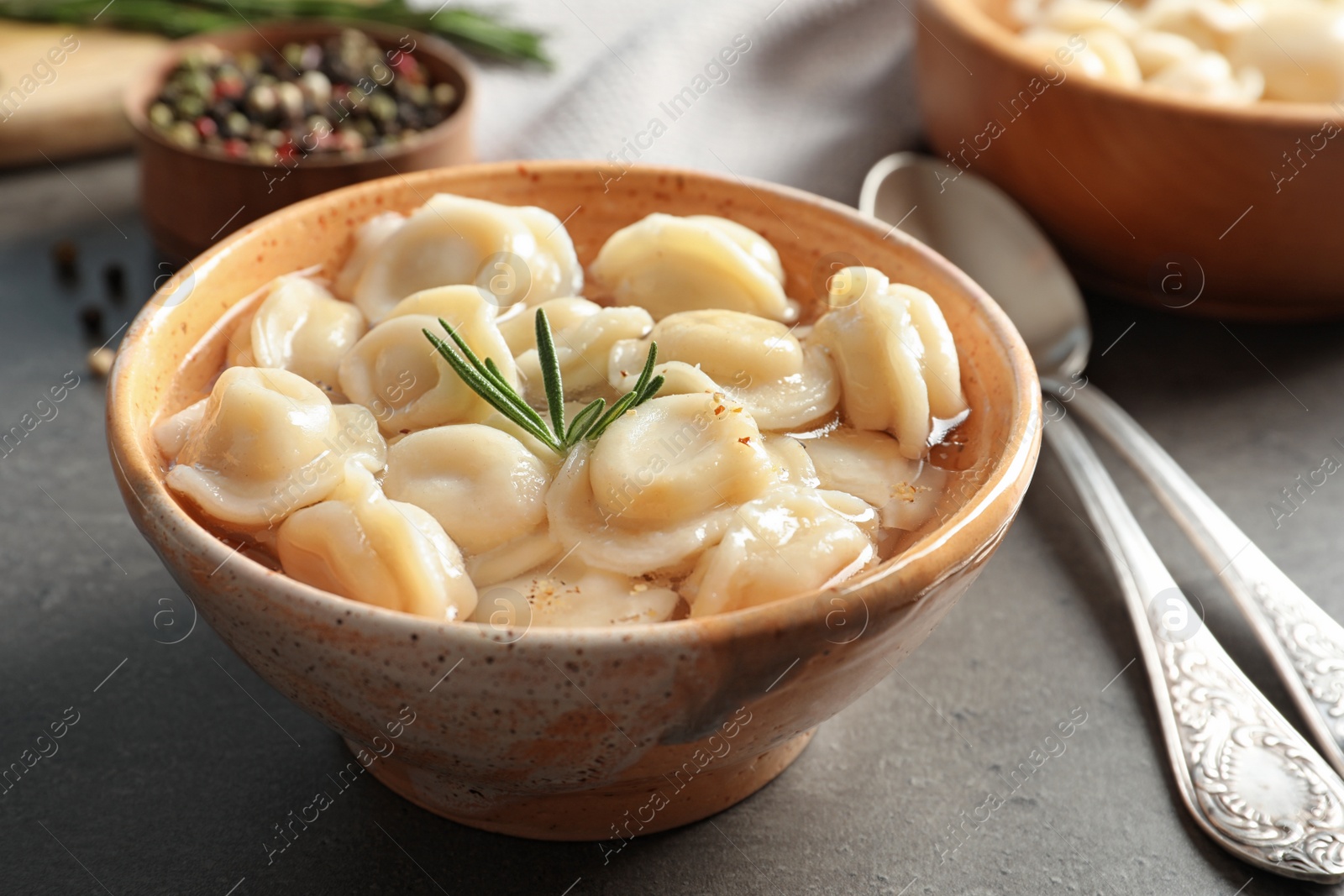 Photo of Bowl of tasty dumplings in broth served on grey table