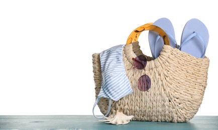 Bag with different beach objects on turquoise wooden table against white background