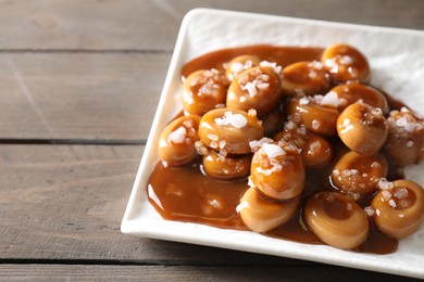 Plate with tasty candies, caramel sauce and salt on wooden table, closeup. Space for text