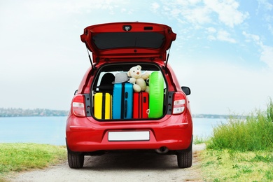 Photo of Suitcases, toys and hat in car trunk on riverside