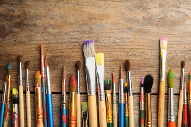 Different paint brushes on wooden background, top view with space for text