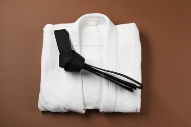 Photo of Black karate belt and kimono on brown background, top view