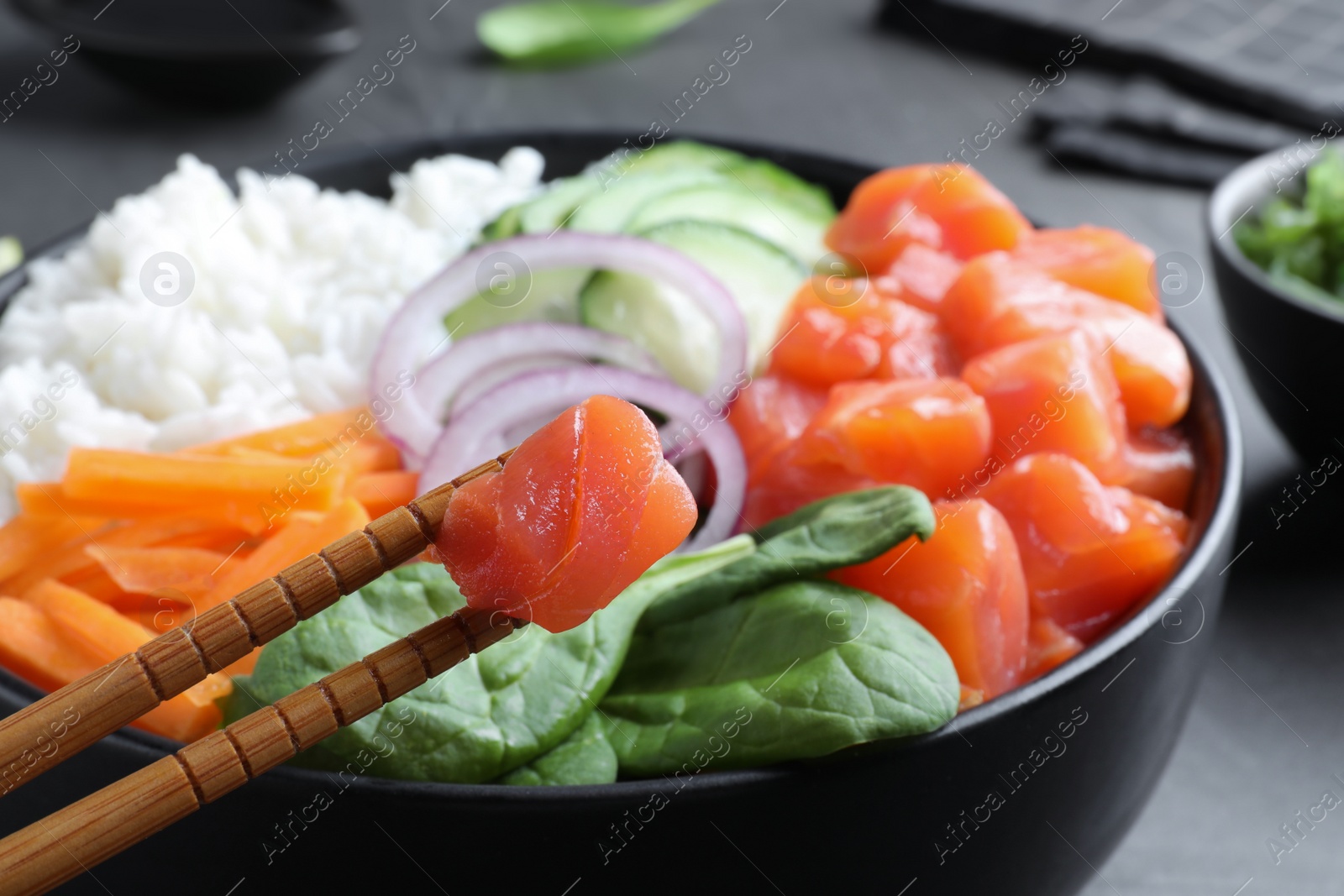 Photo of Wooden chopsticks with piece of salmon over delicious poke bowl on table, closeup