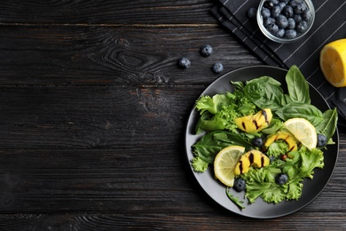 Delicious avocado salad with lemon and blueberries on black wooden table, flat lay. Space for text