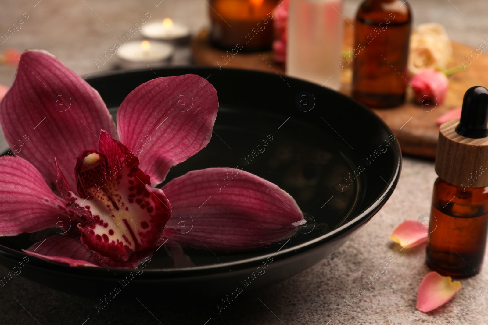 Photo of Bowl of essential oil and beautiful flower on grey table, closeup. Aromatherapy treatment