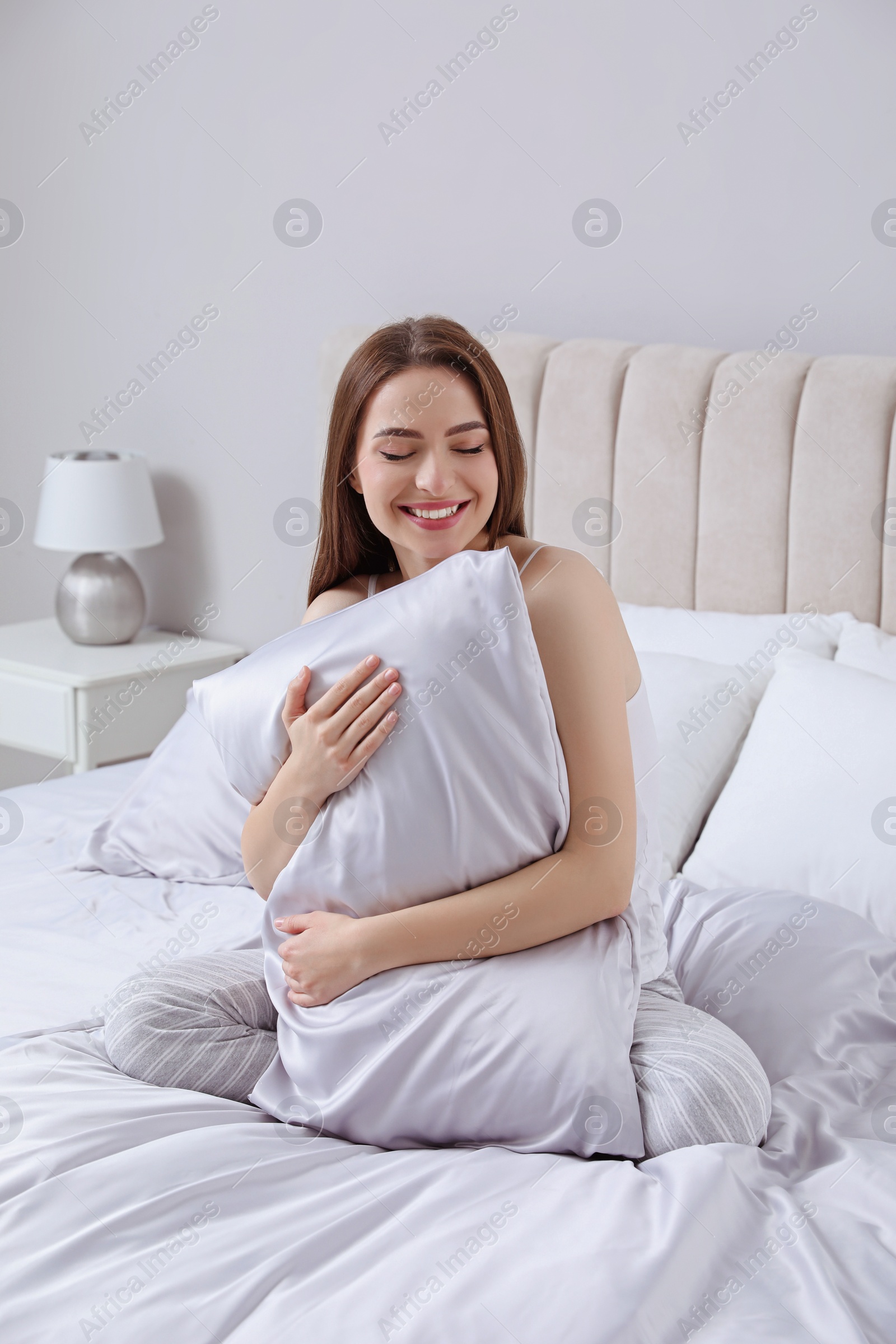 Photo of Young woman hugging pillow on comfortable bed with silky linens