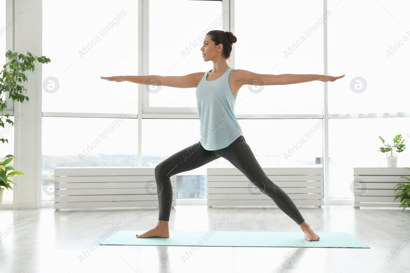 Photo of Young woman practicing warrior asana in yoga studio. Virabhadrasana pose